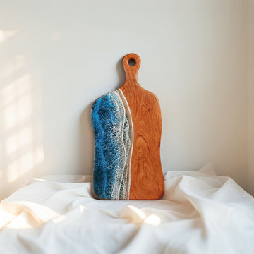 Wooden cutting board with blue and white resin design on a white fabric background