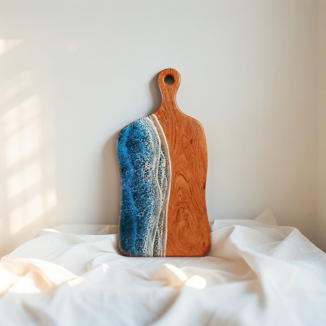 Wooden cutting board with blue and white resin design on a white fabric background
