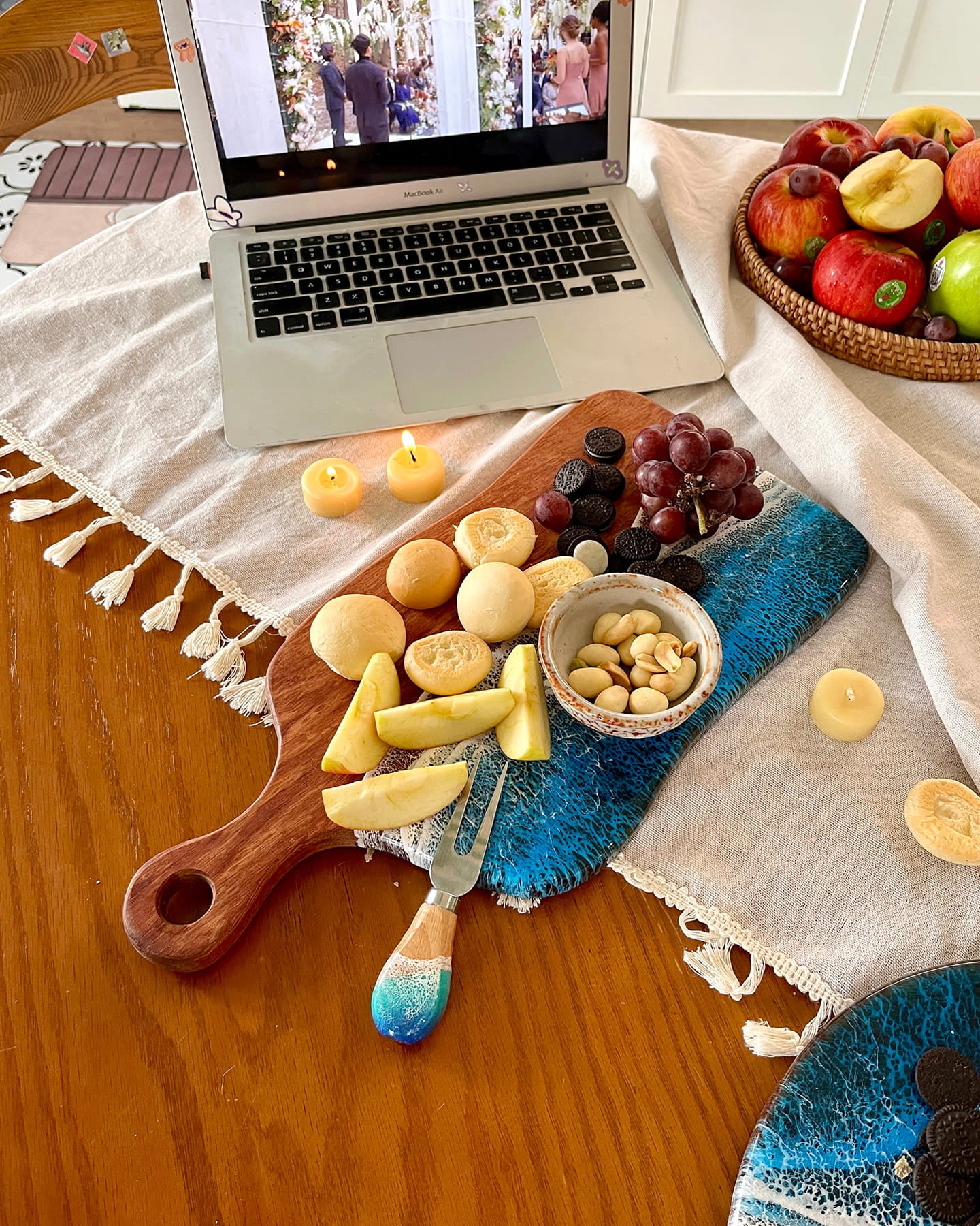 Laptop on a table with a charcuterie board and fruits