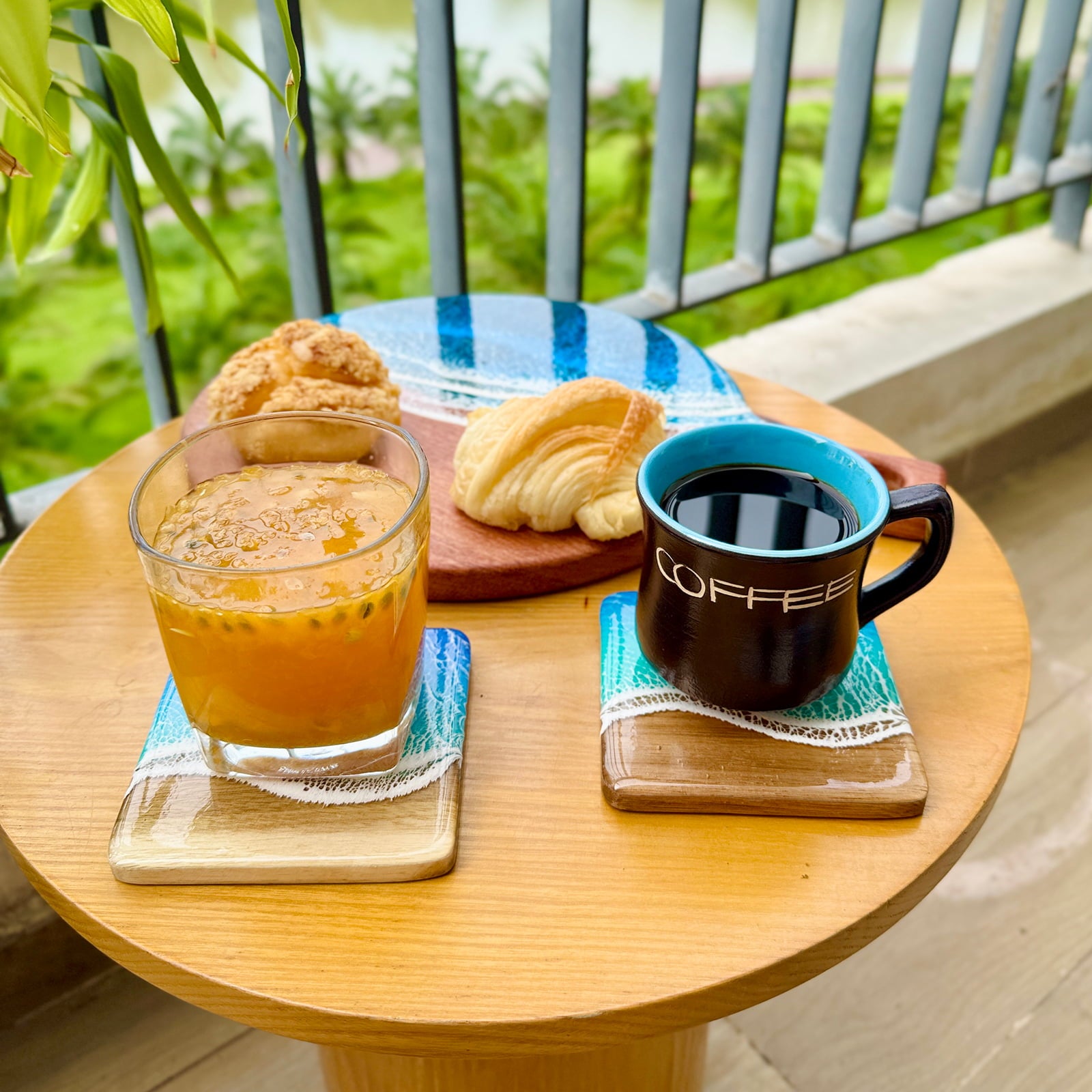 Glass of orange juice and coffee mug on a wooden table with pastries, outdoor setting.
